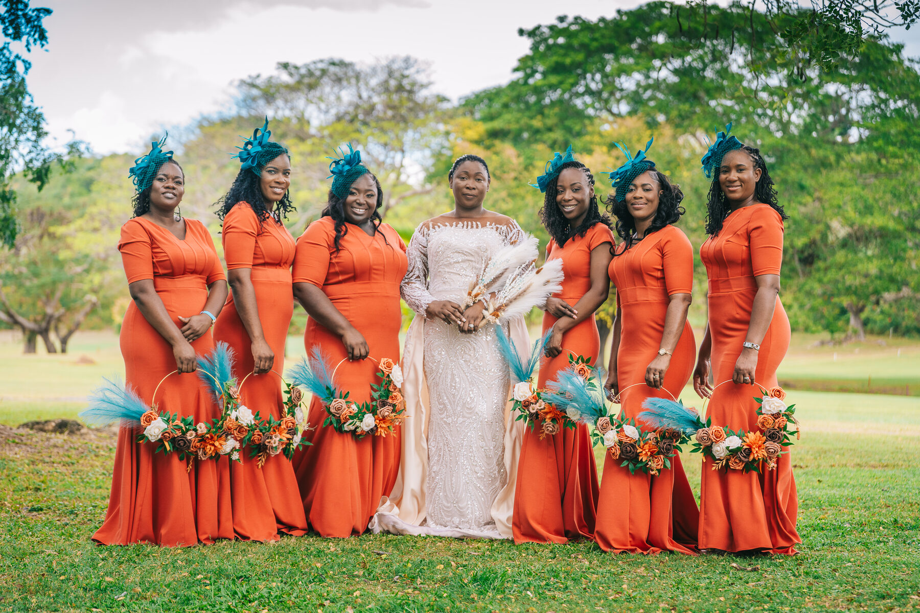 The full bridal party in coral dresses and suits under a large tree