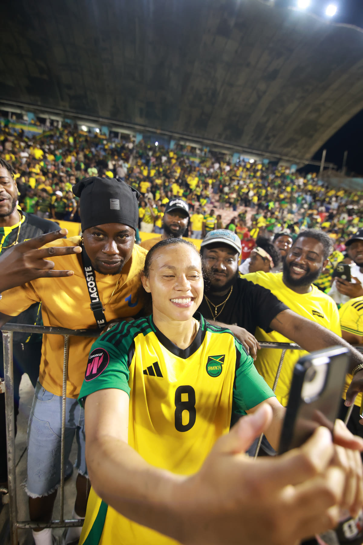 A Reggae Girlz player takes a selfie with supporters at the National Stadium