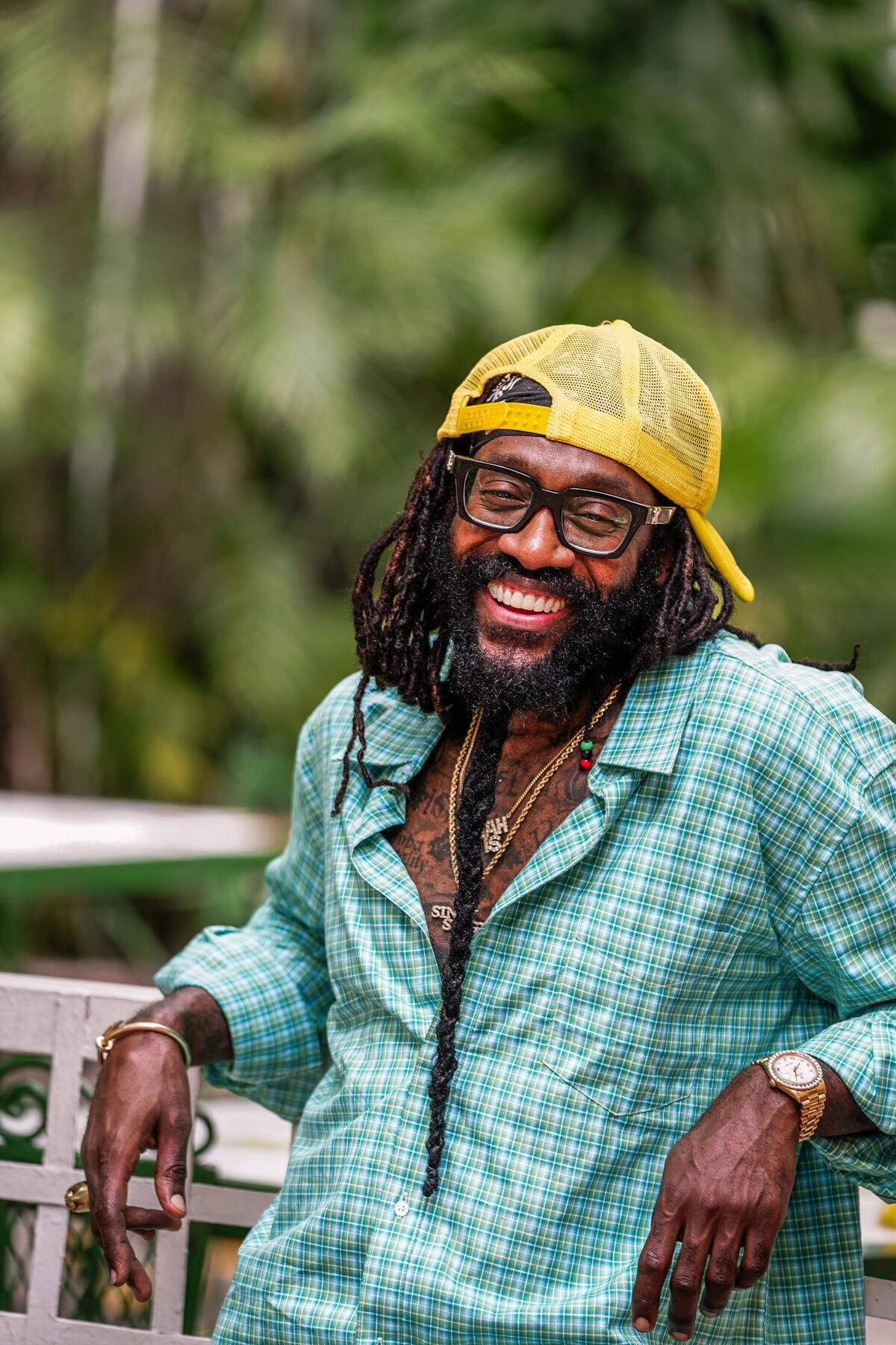 A man with locs and glasses leans on a railing, smiling outdoors