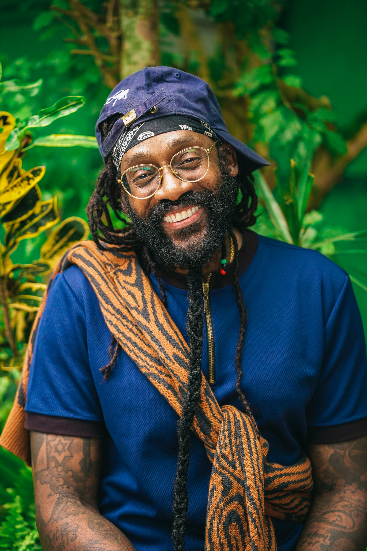 A man with locs in a blue shirt against rich green foliage