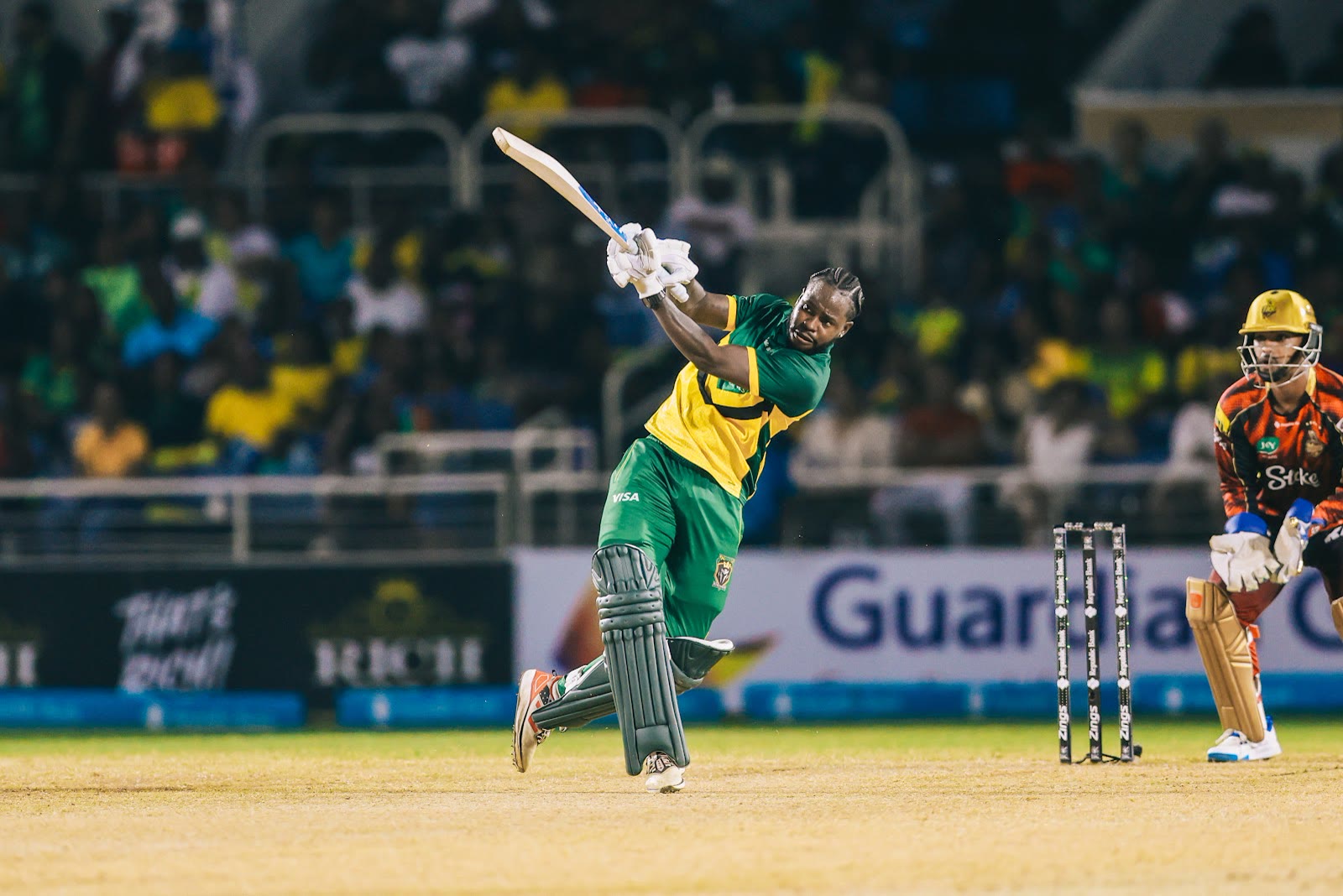 A Jamaica Kingsmen batter swings hard under the Sabina Park floodlights as the Trinbago Knight Riders keeper watches