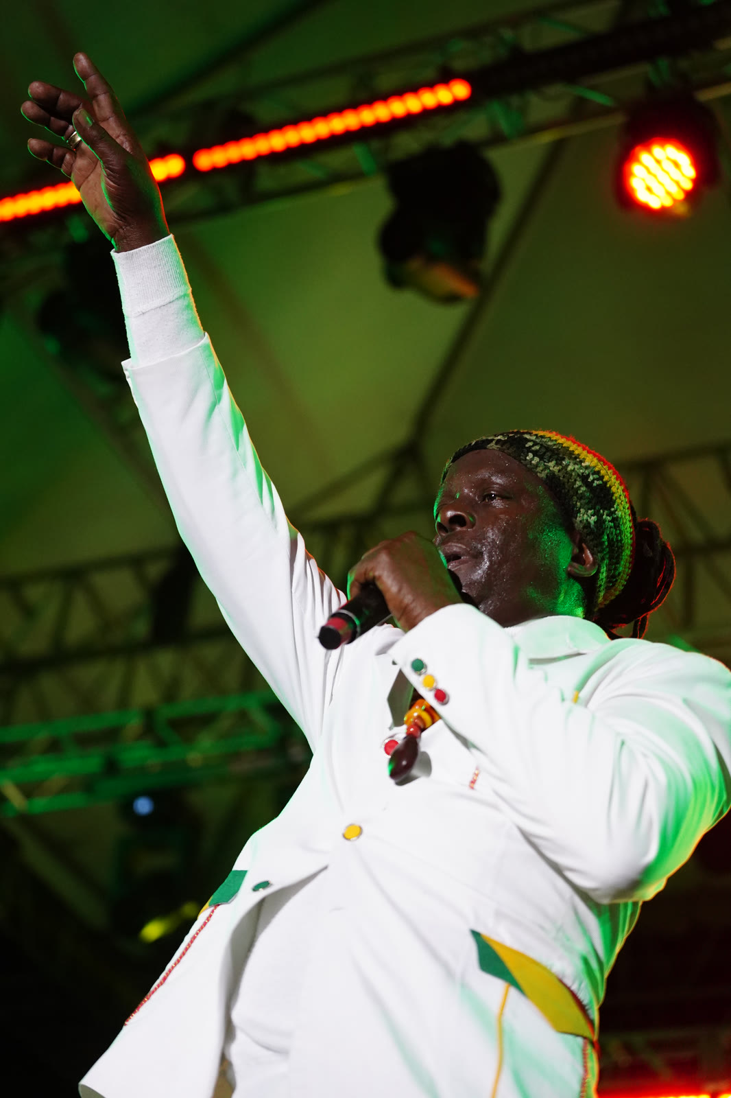 An artist in a white suit raises his arm mid-song under the stage lights