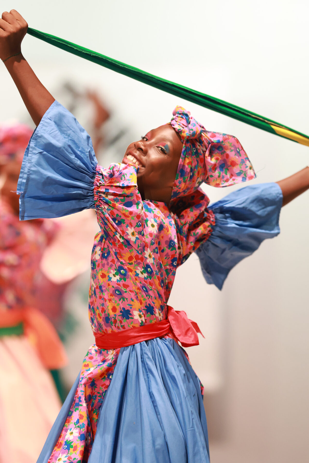 A performer in a vivid patterned costume moves across the stage with a ribbon