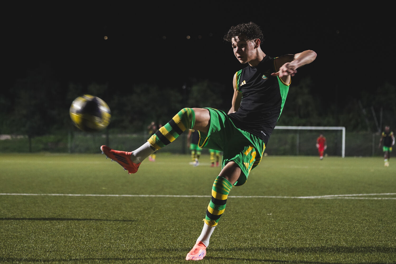 A footballer in Jamaica green and gold strikes a bicycle kick against the night stadium