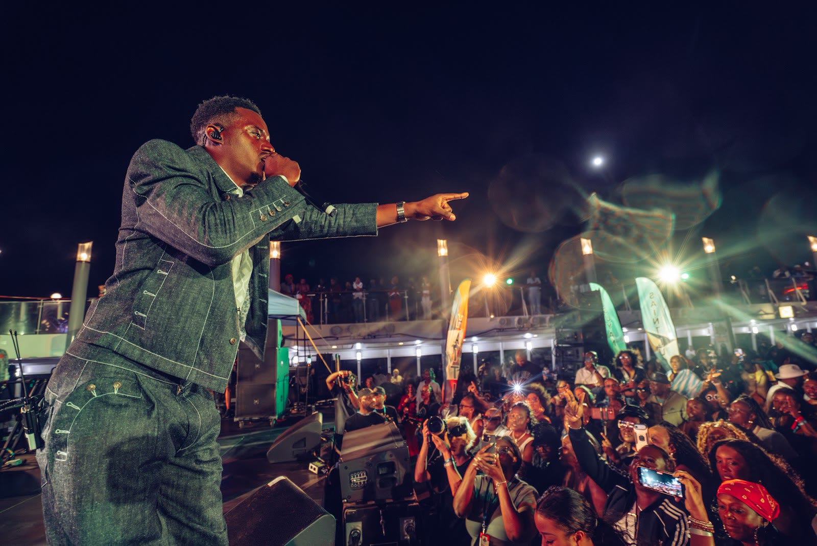 Romain Virgo points to the crowd from the pool-deck stage at night