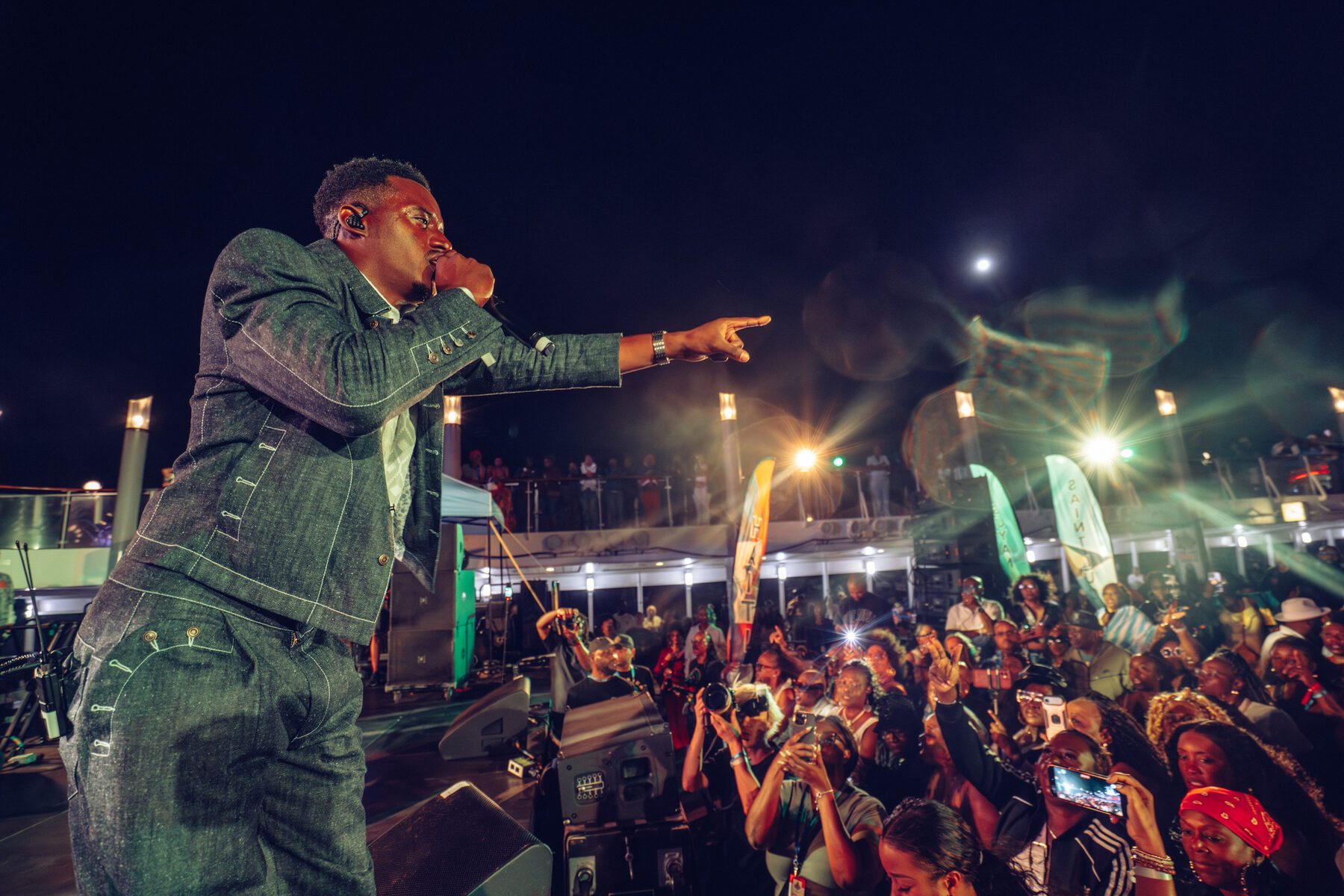 An artist in a denim suit performs to a packed night crowd holding up phones
