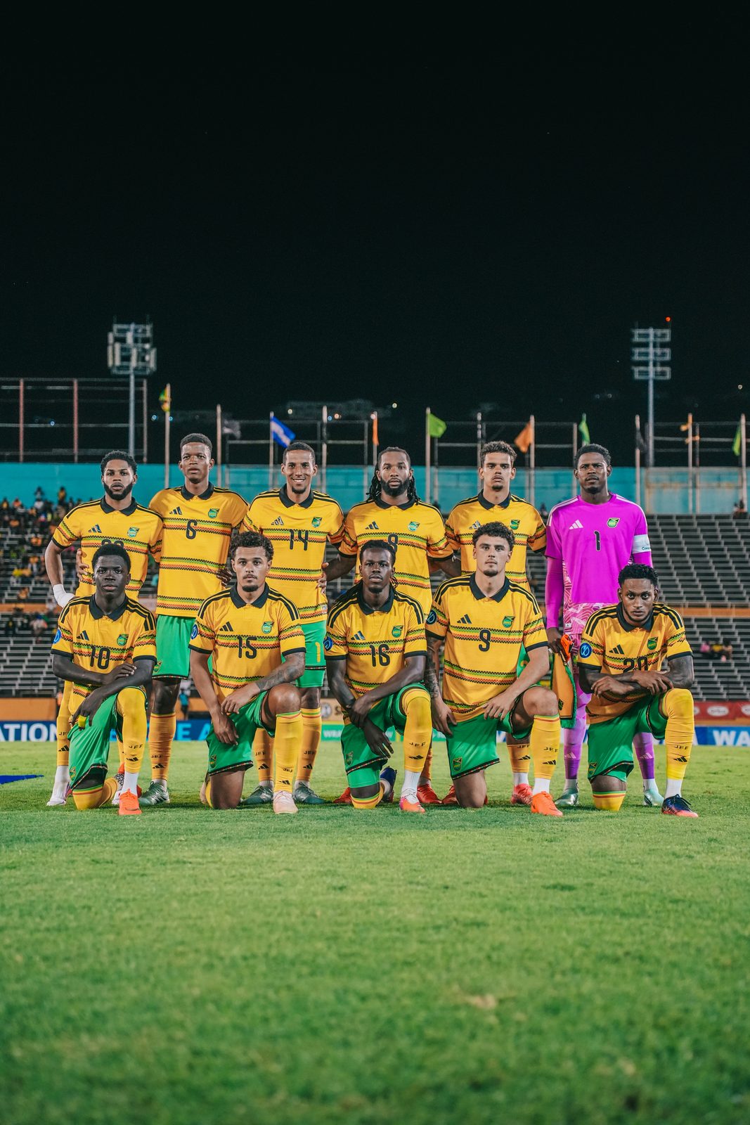 The Reggae Boyz line-up photographed on the pitch at night, with open space above the players