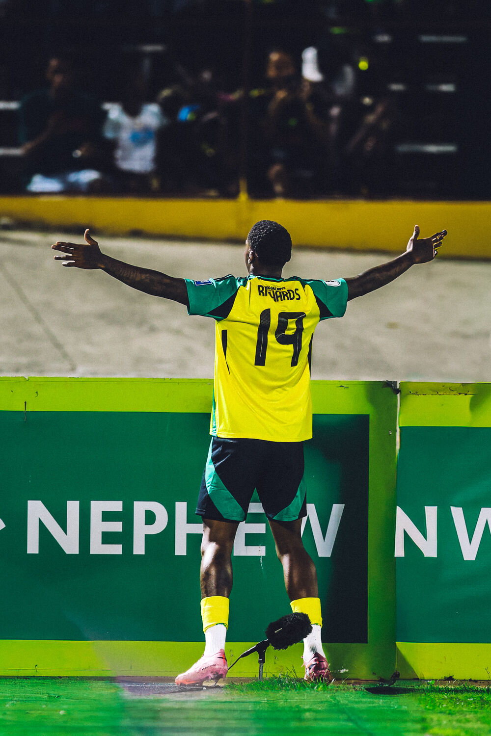 A player celebrates arms-wide under the Premier League lights at the National Stadium
