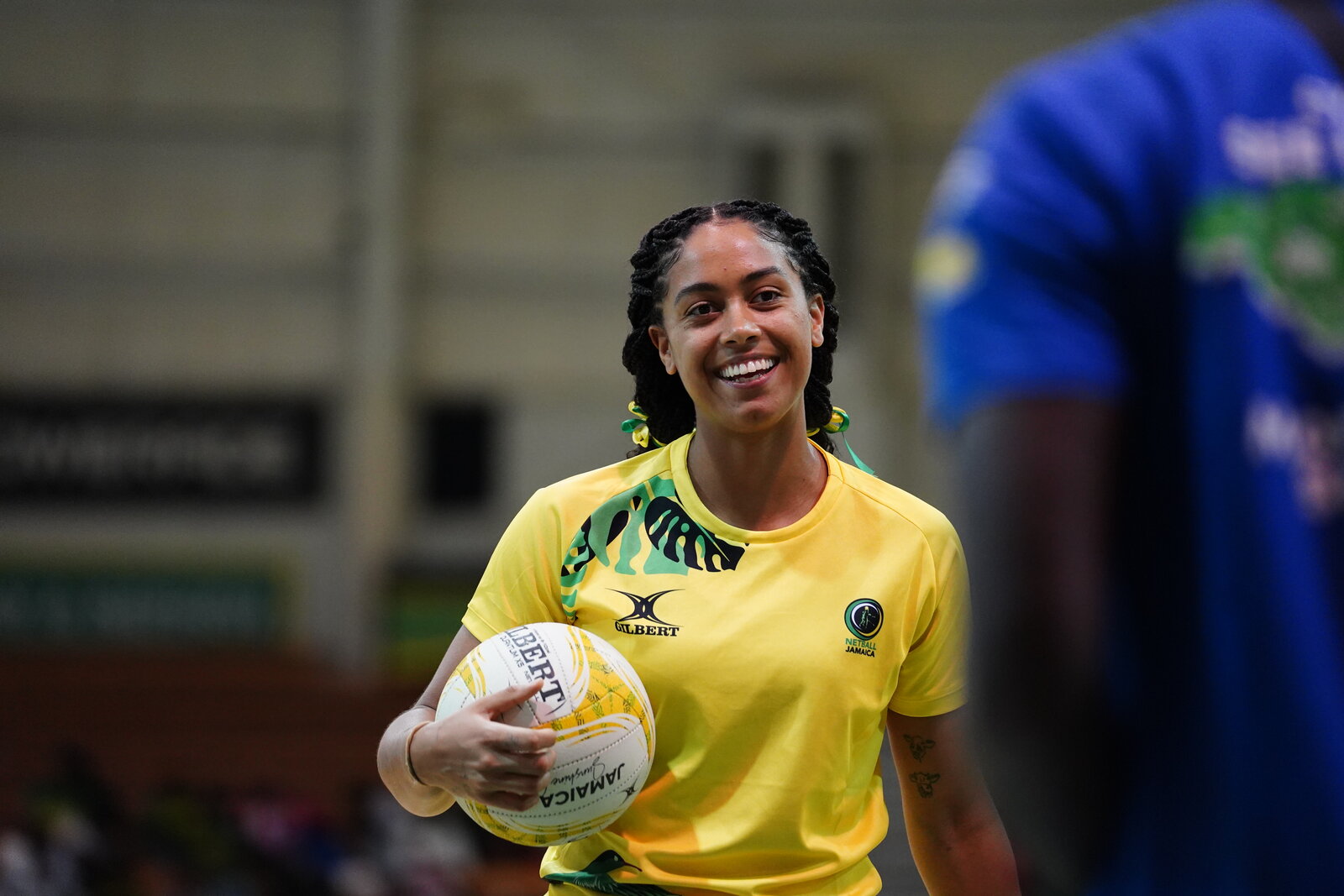 A smiling Jamaica netballer holds the ball at her hip