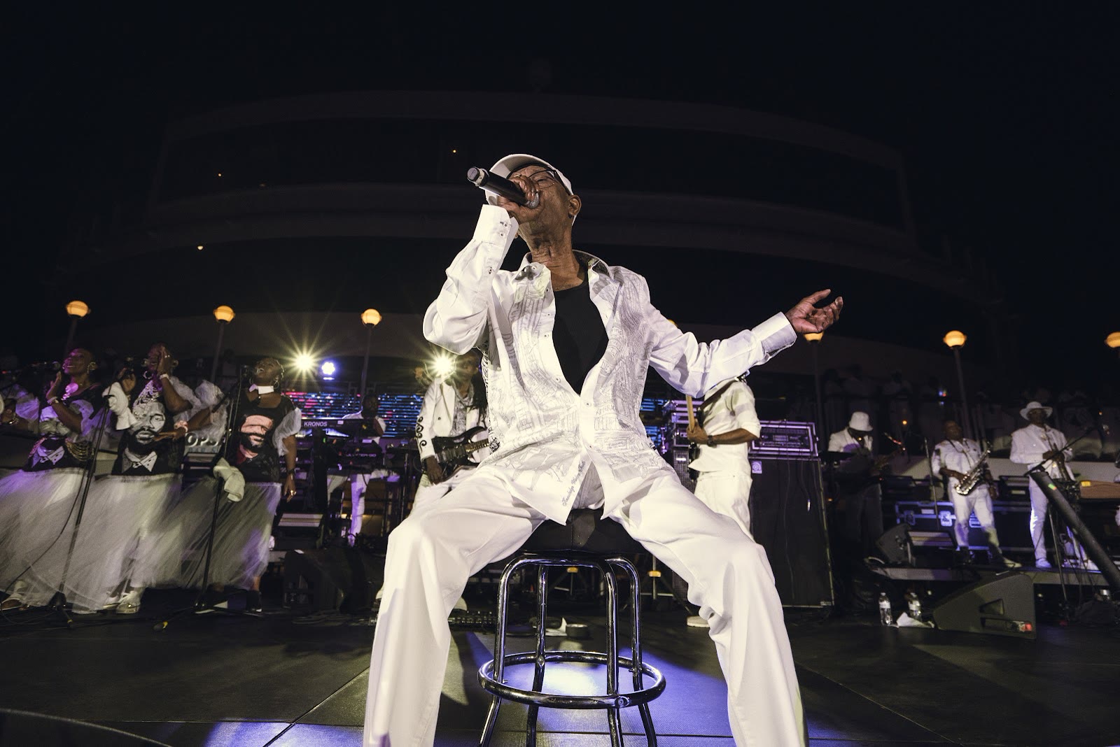 Beres Hammond performs seated on a stool in white with his band behind him