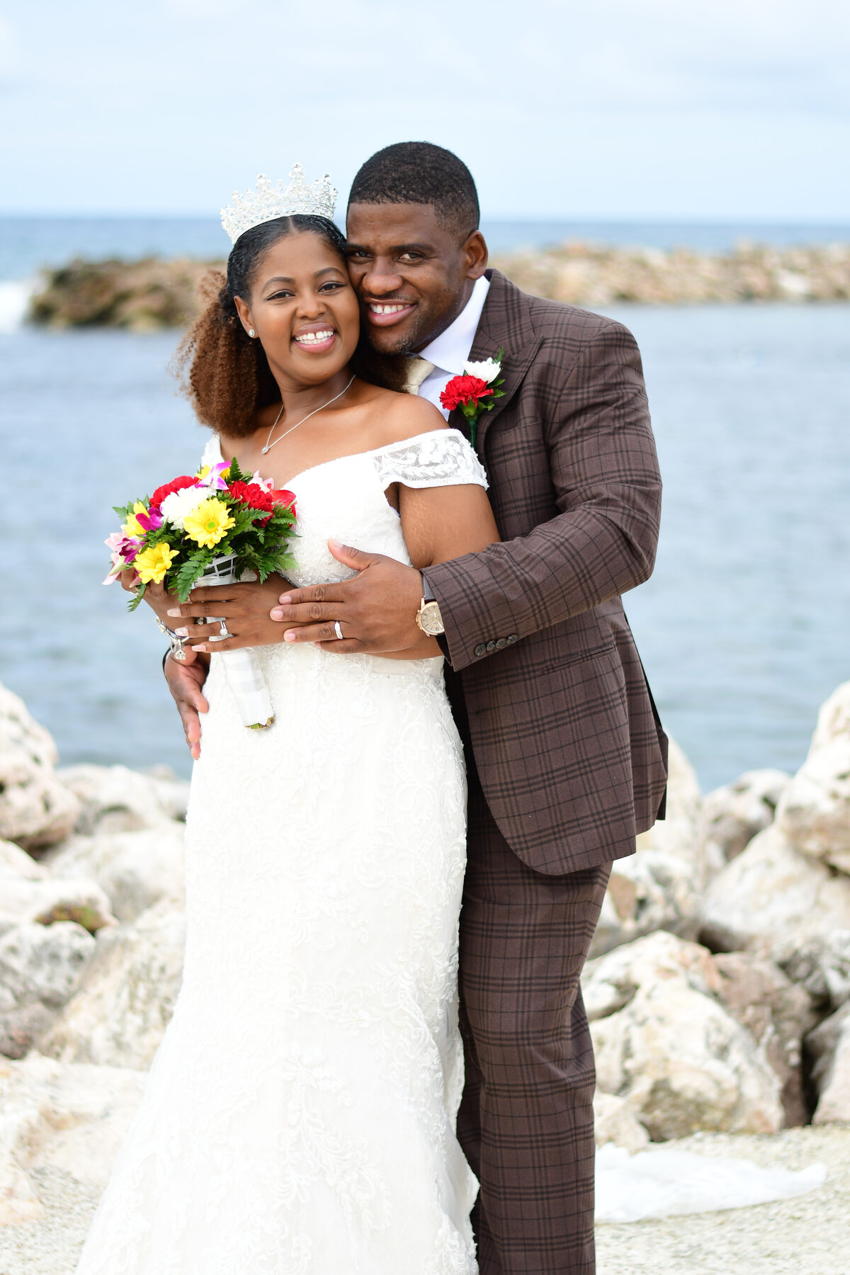 A bride and groom hand in hand with a bouquet on the rocks