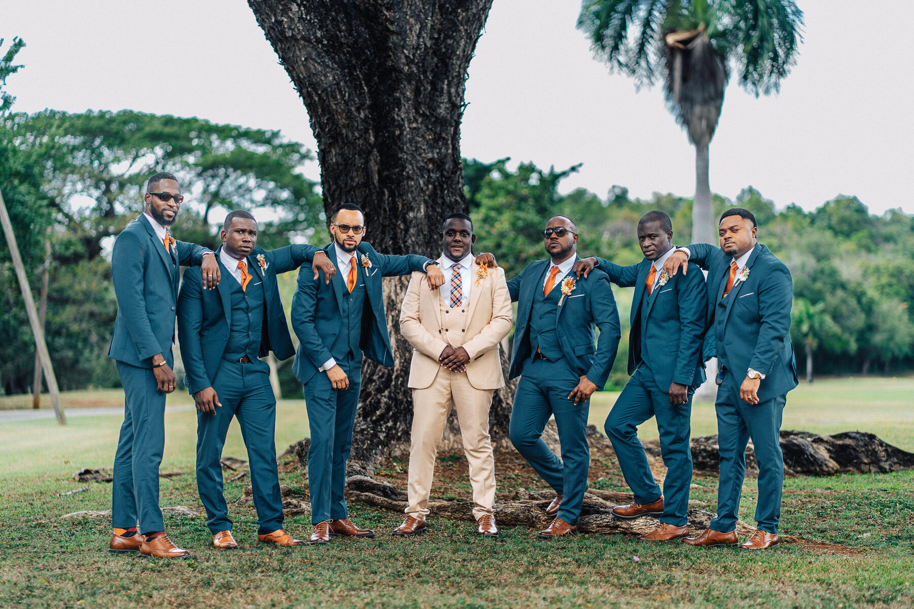 The groom and his groomsmen in blue suits lined up under trees