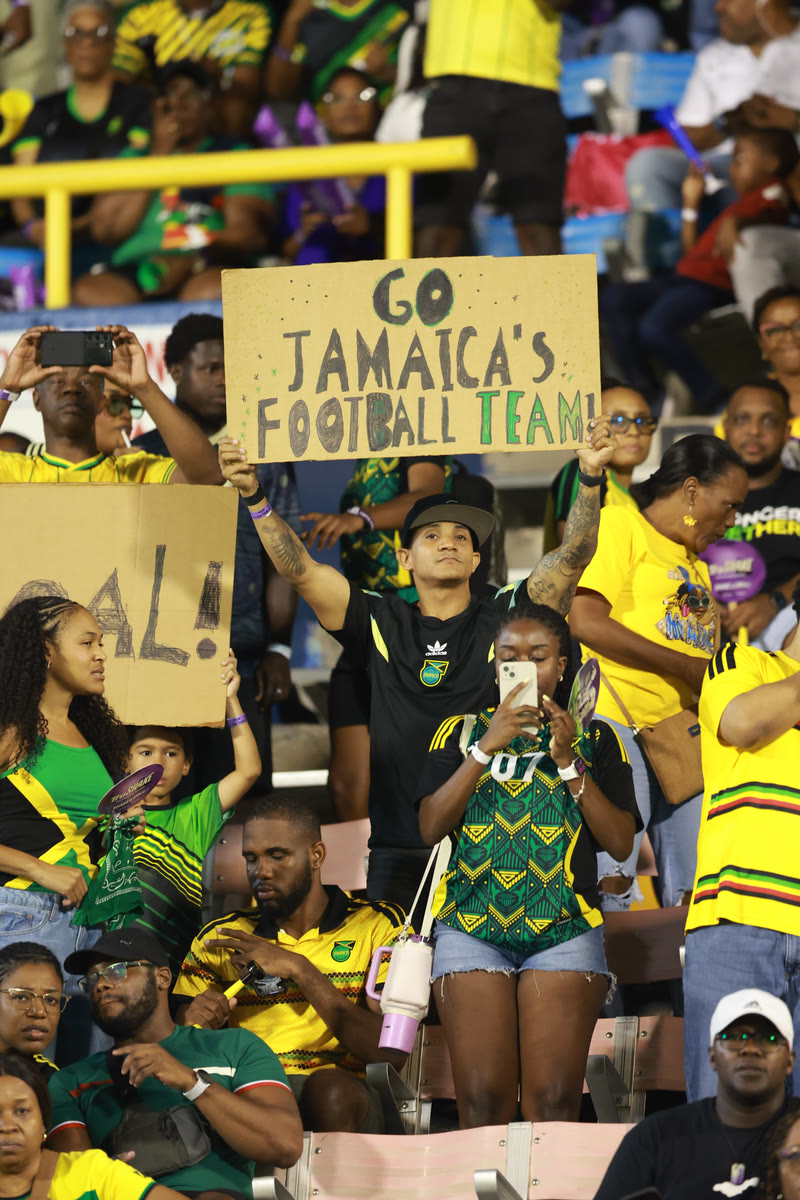 Supporters in the stands hold up a sign that reads Go Jamaica’s football team