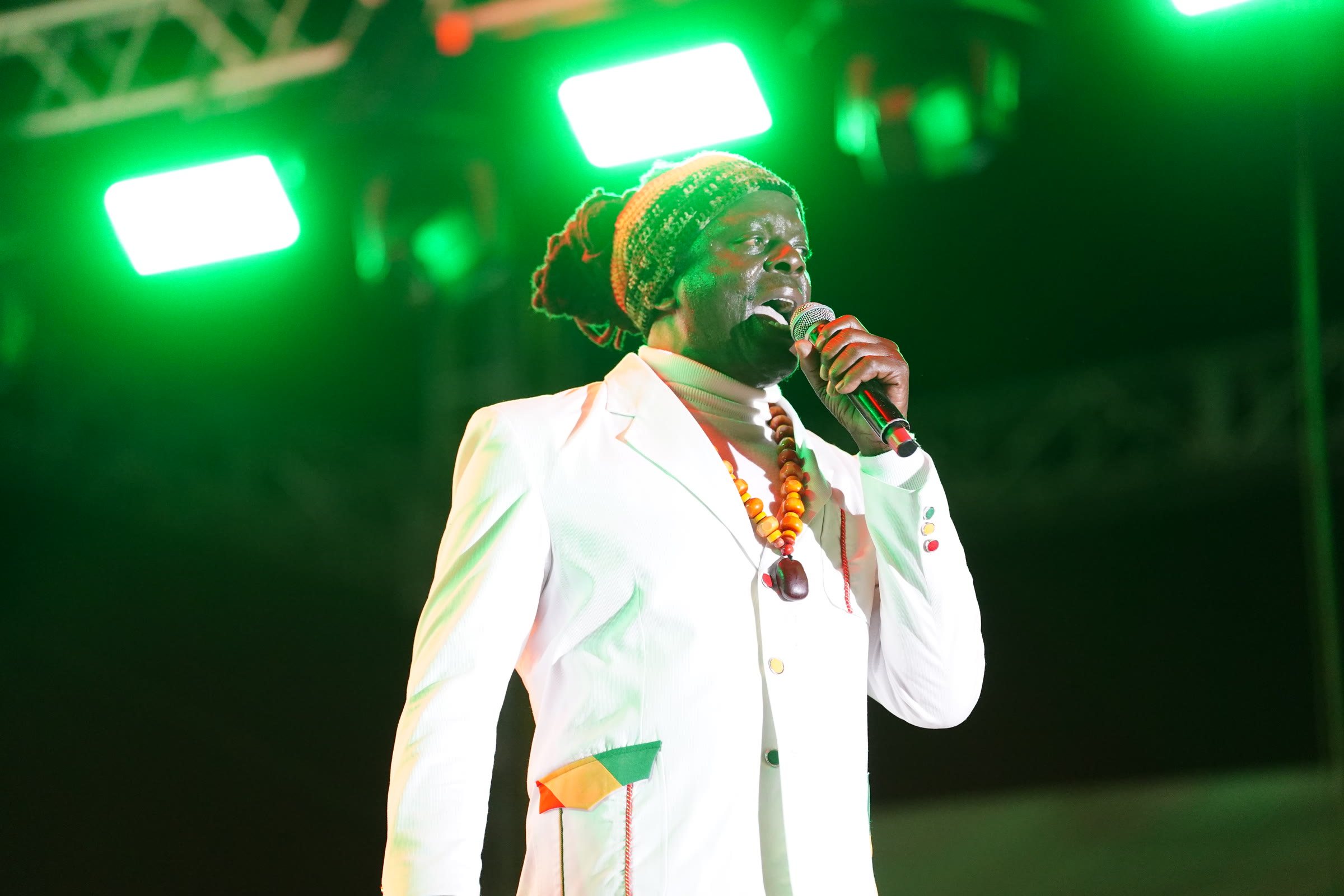 An artist in a white suit sings under green stage light