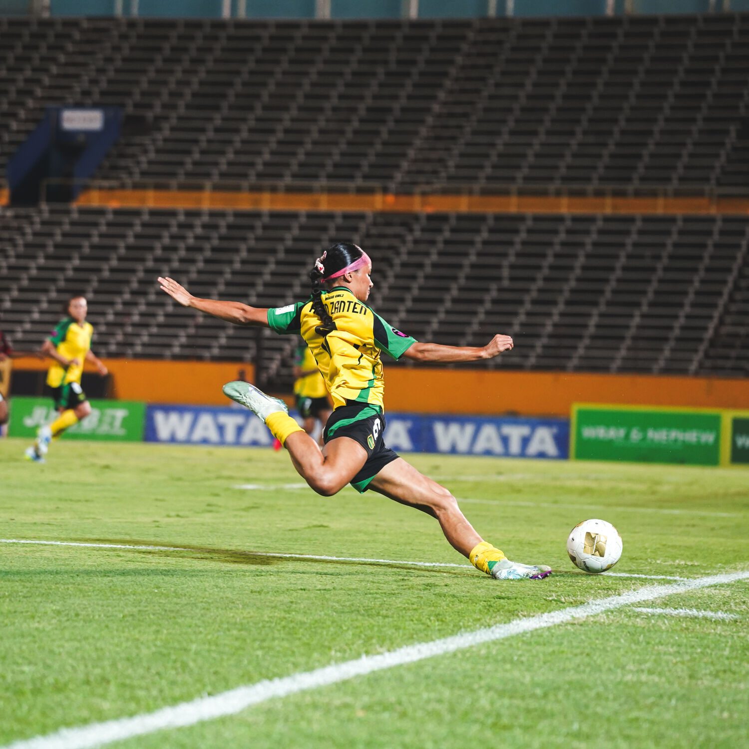 A Reggae Girlz player strikes the ball mid-stride on the pitch