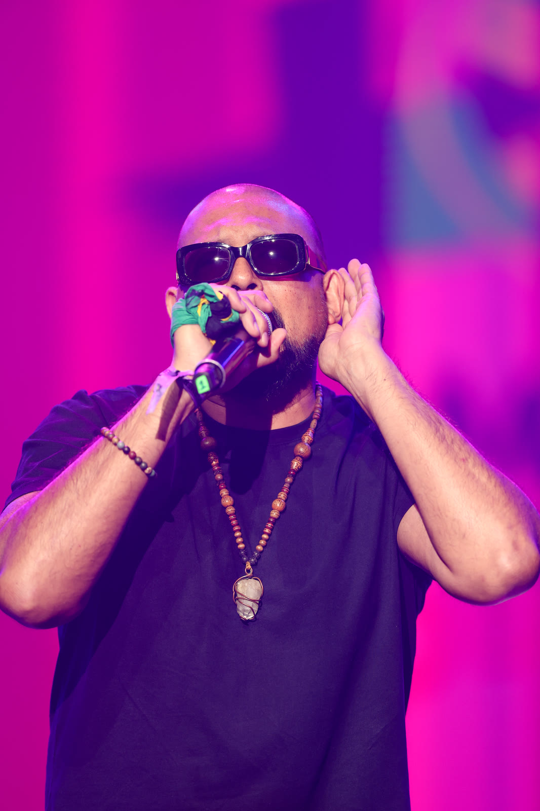 An artist in dark shades cups his ear as he sings under pink light