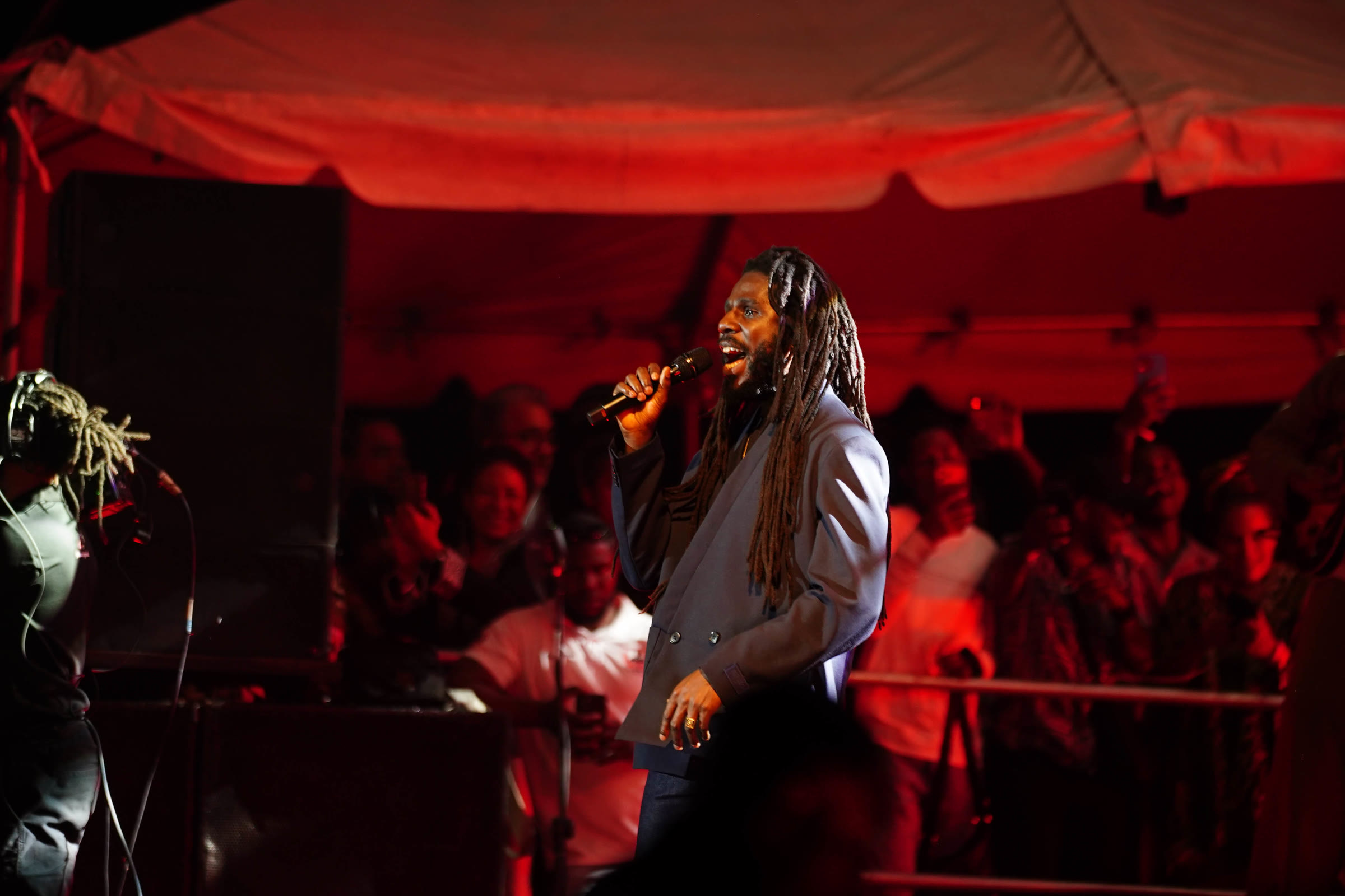 Chronixx sings under a red-lit canopy with the crowd behind him