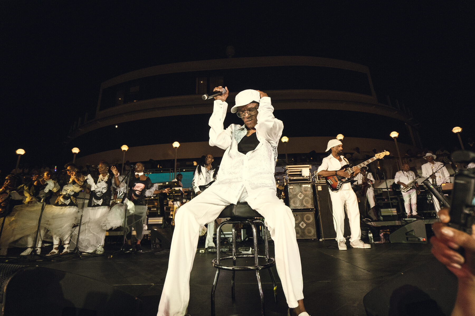 A veteran reggae artist performs seated in all white with his band behind him