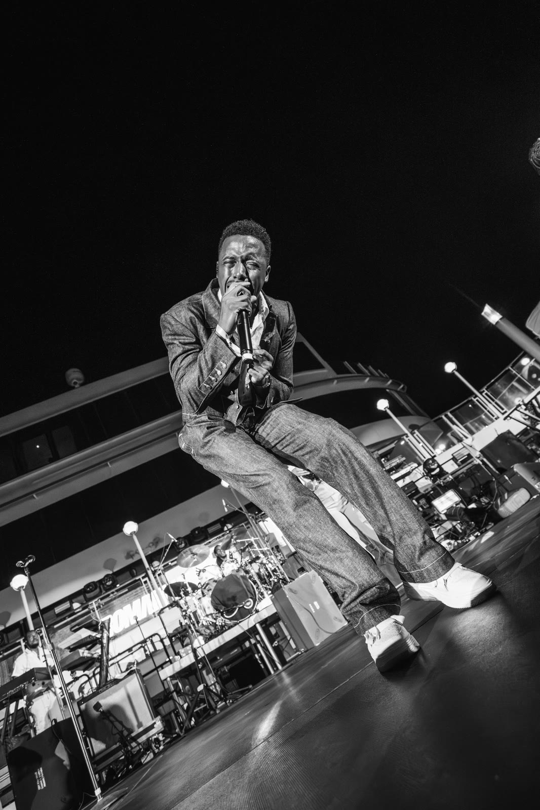Romain Virgo sits on the edge of the stage in black and white
