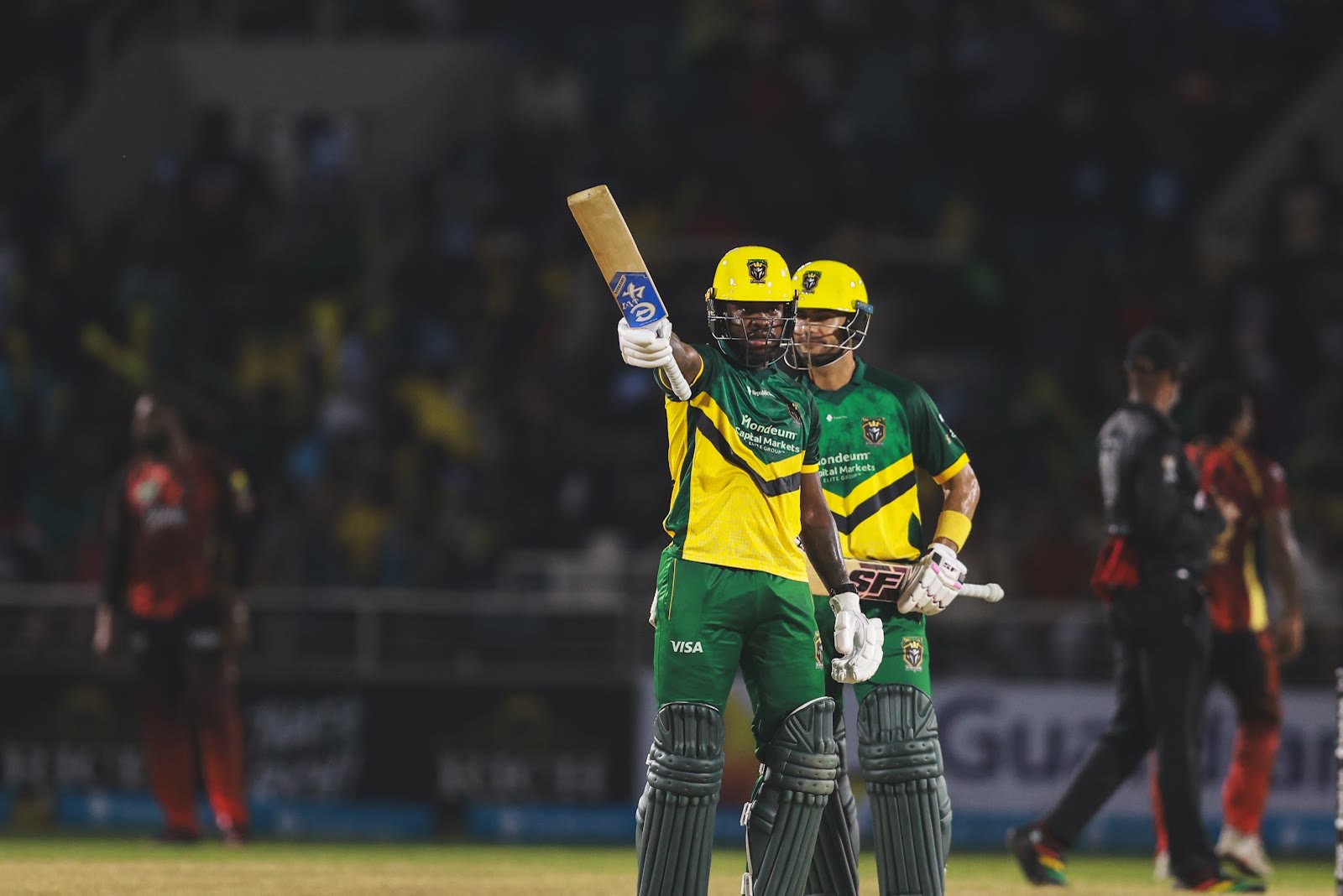 A Kingsmen batter in a yellow helmet raises his bat beside his partner