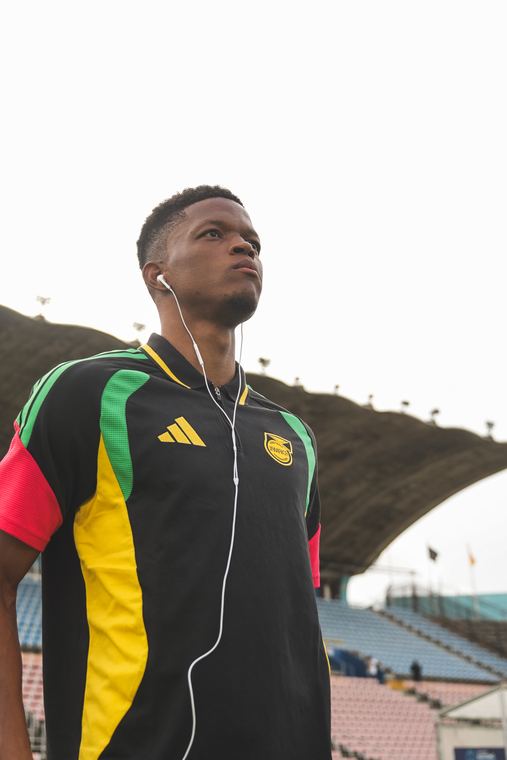 A Reggae Boyz player in the travel top walks the pitch before kick-off