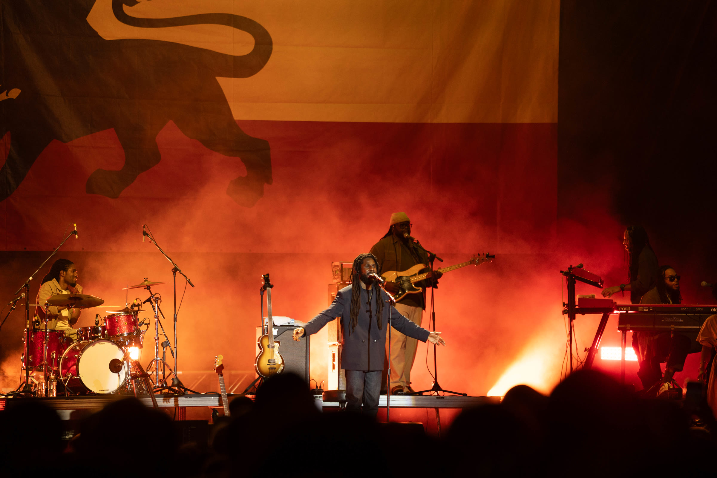 Chronixx and his band on an orange-lit stage, a lion banner behind them