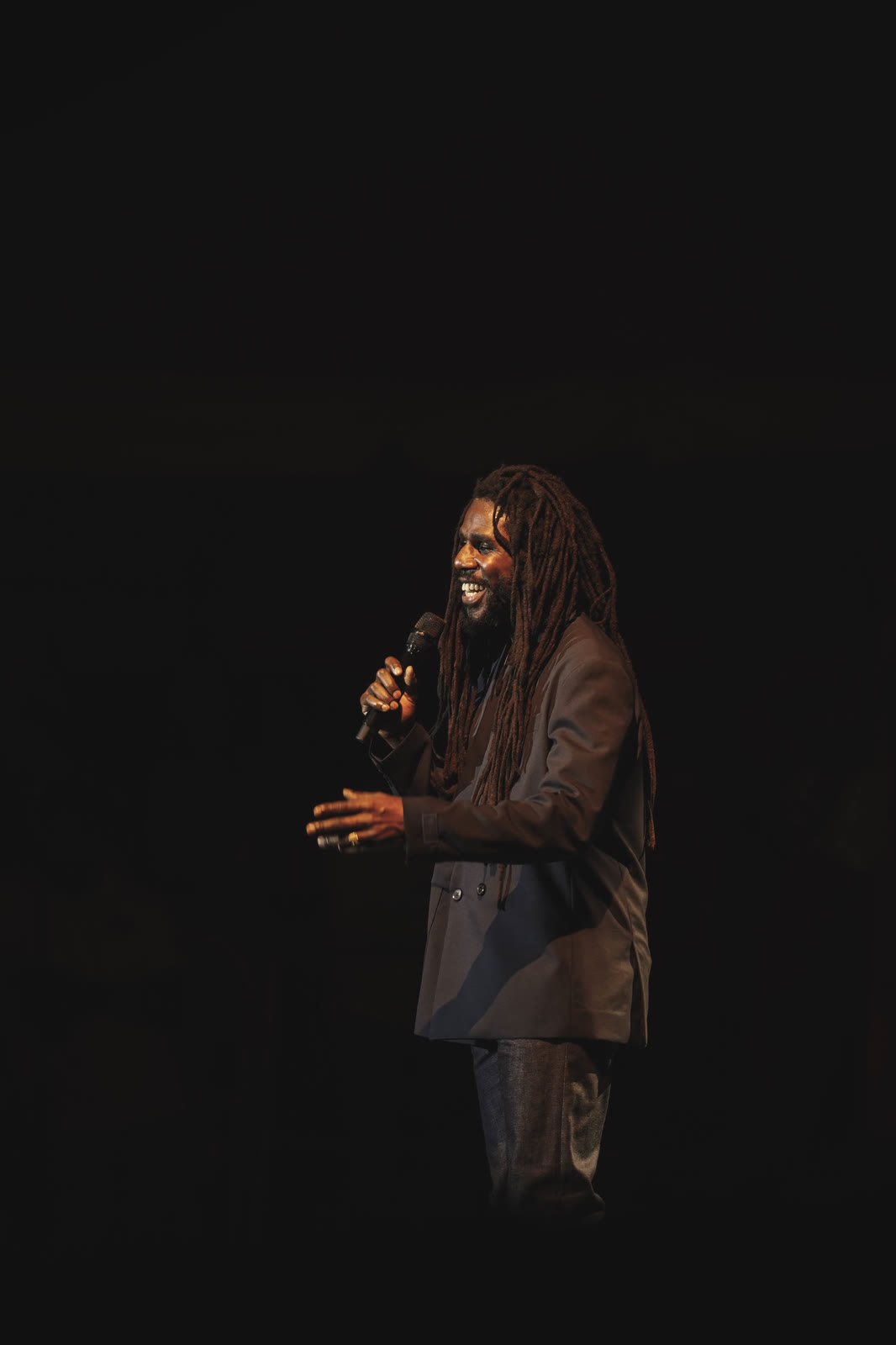 Chronixx smiles at the mic on a dark stage