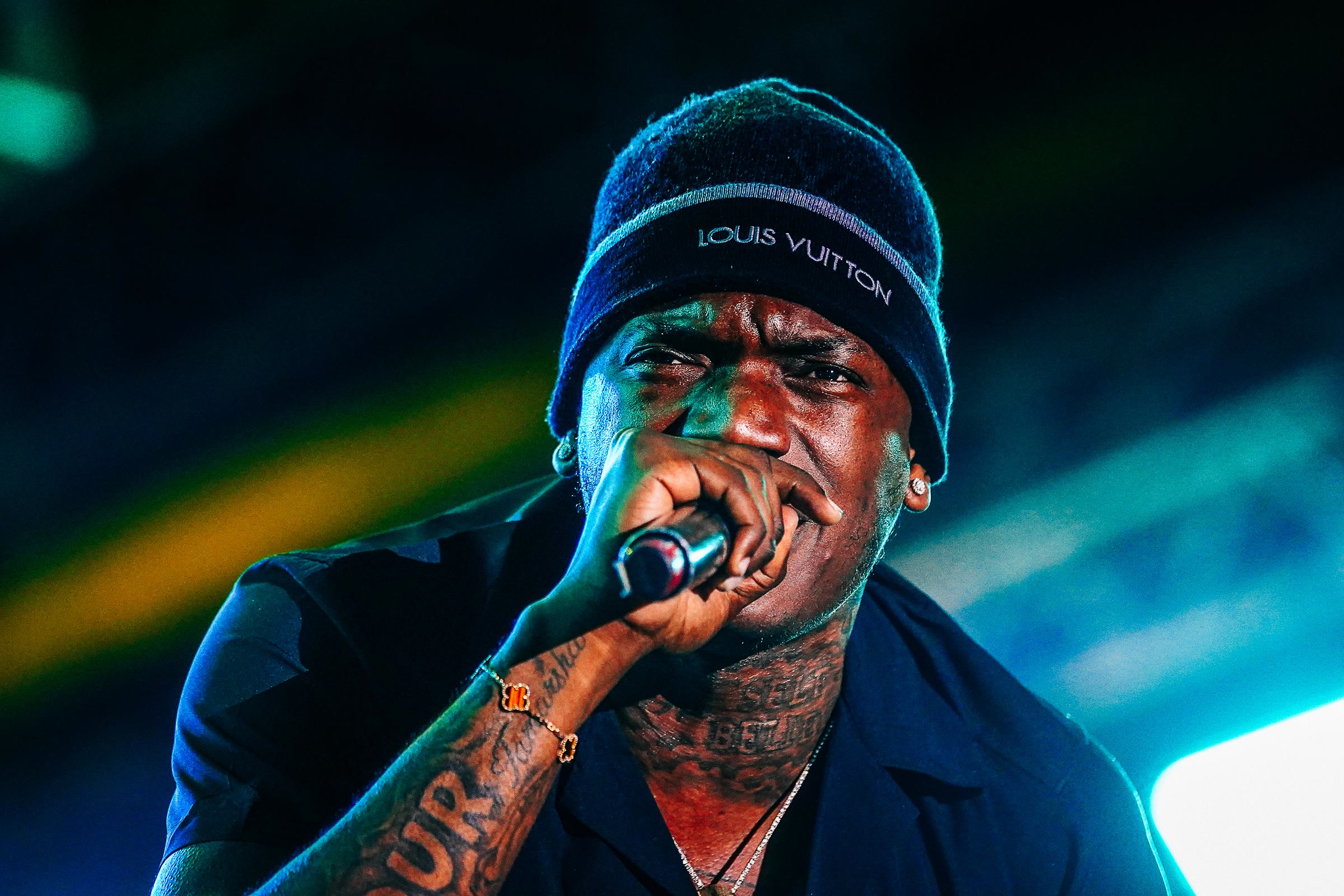 An artist in a dark beanie sings into the mic under blue stage light
