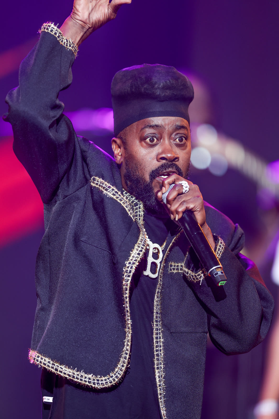 An artist in a black kufi raises his hand as he sings